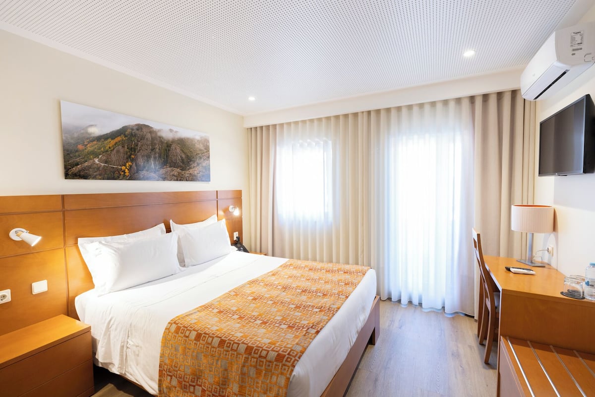 A hotel room with a large bed, a desk with a lamp, a TV, and a painting on the wall.
