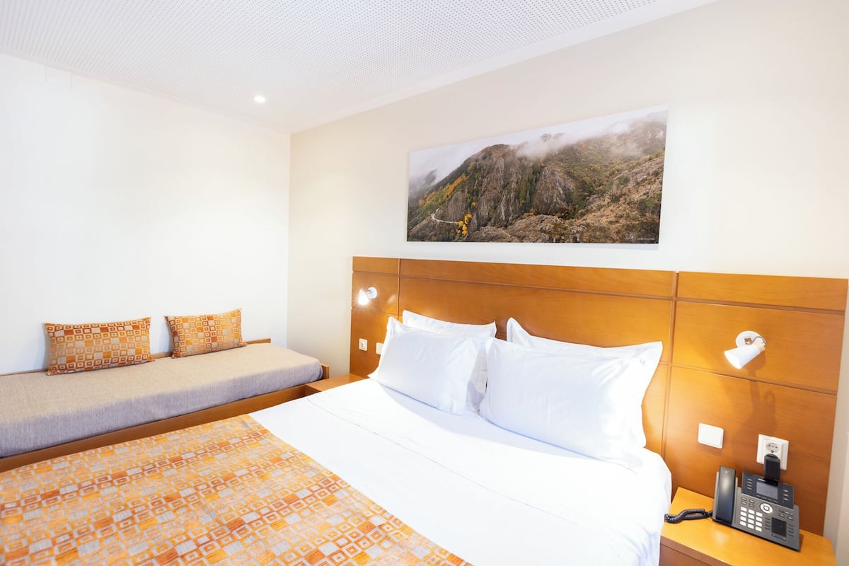 A hotel room with a bed, a sofa, a telephone, and a picture on the wall.