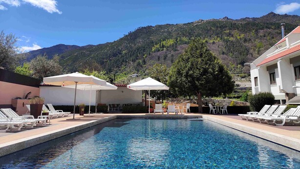 Ein Pool mit Liegestühlen und Sonnenschirmen, mit einem Bergpanorama im Hintergrund.