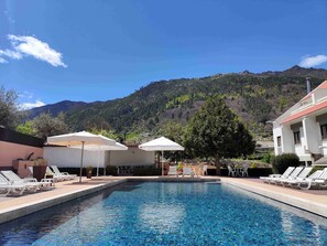 Una piscina con sillones de descanso y sombrillas, con montañas al fondo.