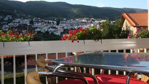 Ein Balkon mit Tisch und Stühlen, der Blick auf eine Stadt mit roten Dächern und einen Berg im Hintergrund bietet.