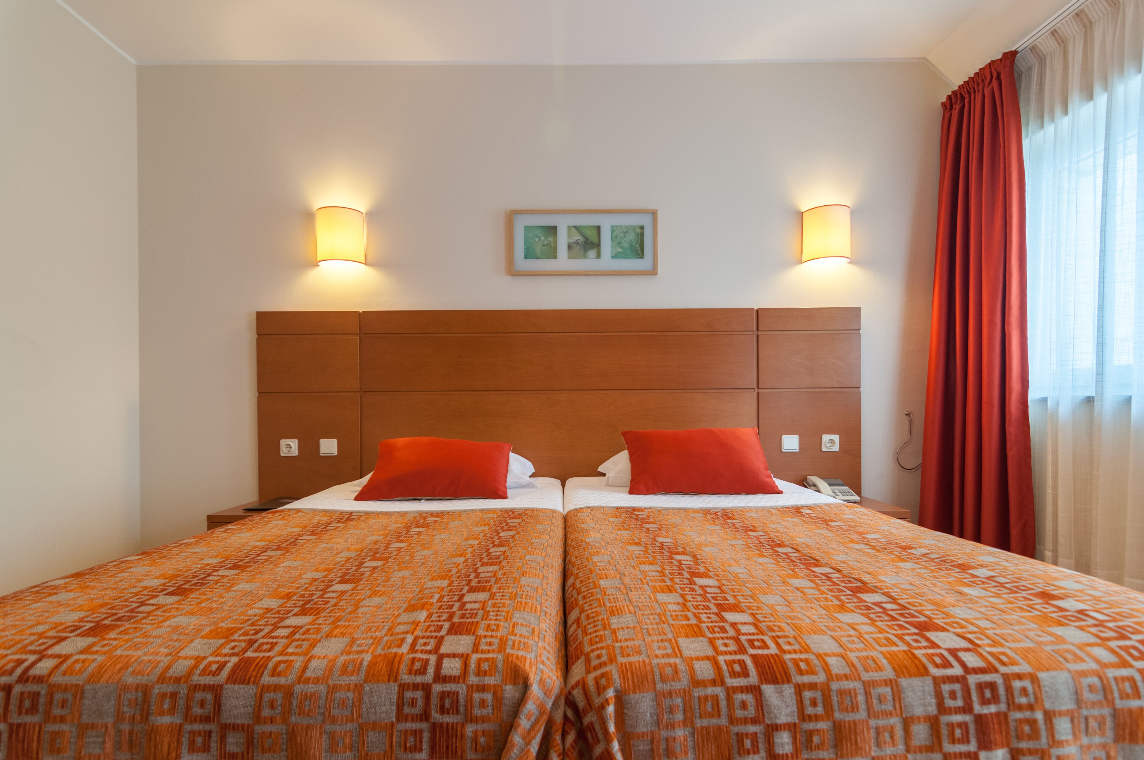 A double room with two beds, each with a patterned bedspread, a wooden headboard, bedside lamps, and a framed picture on the wall.