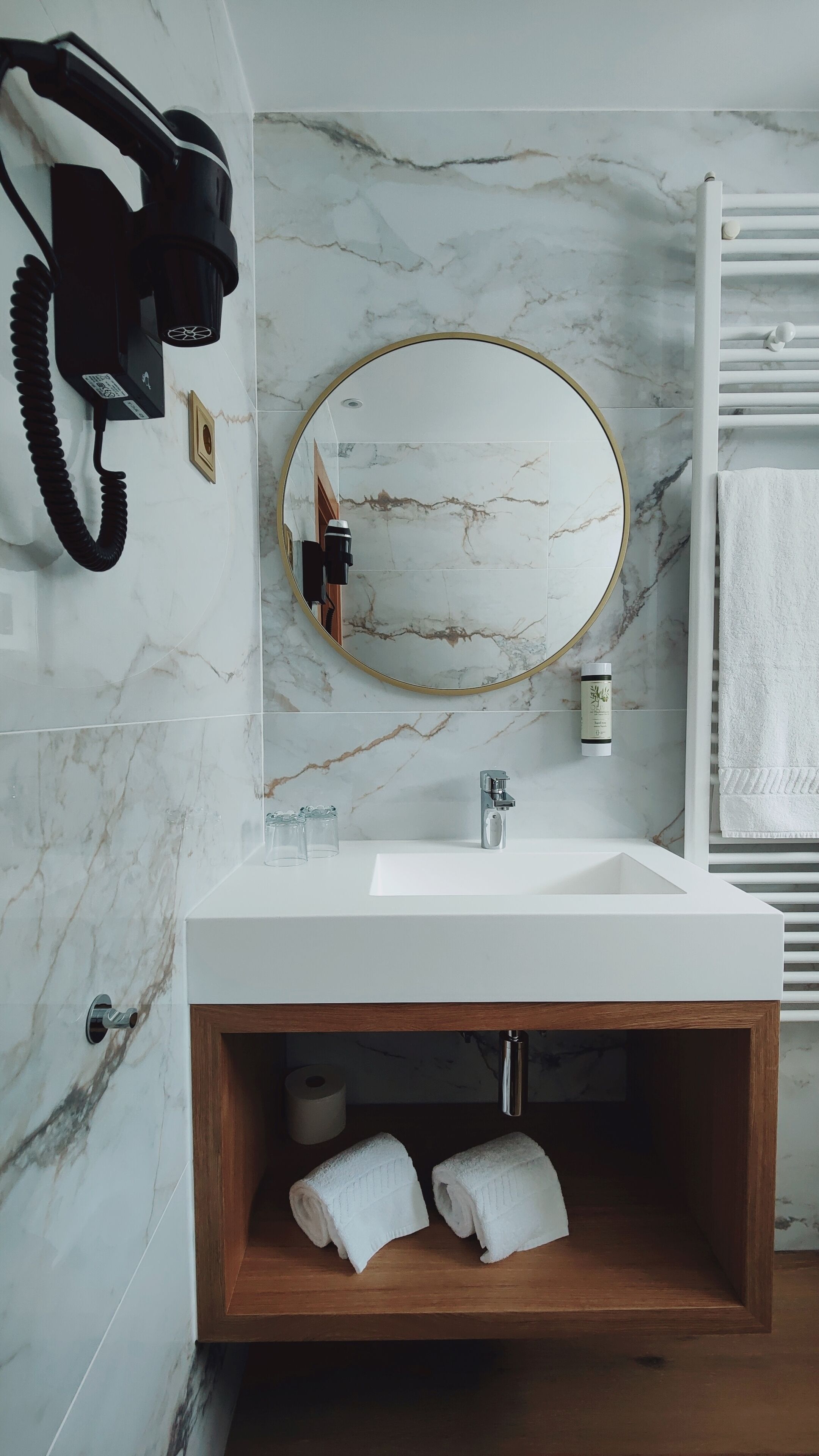 A bathroom with a marble backsplash, a white sink, a wooden vanity, a towel rack, and a black telephone.