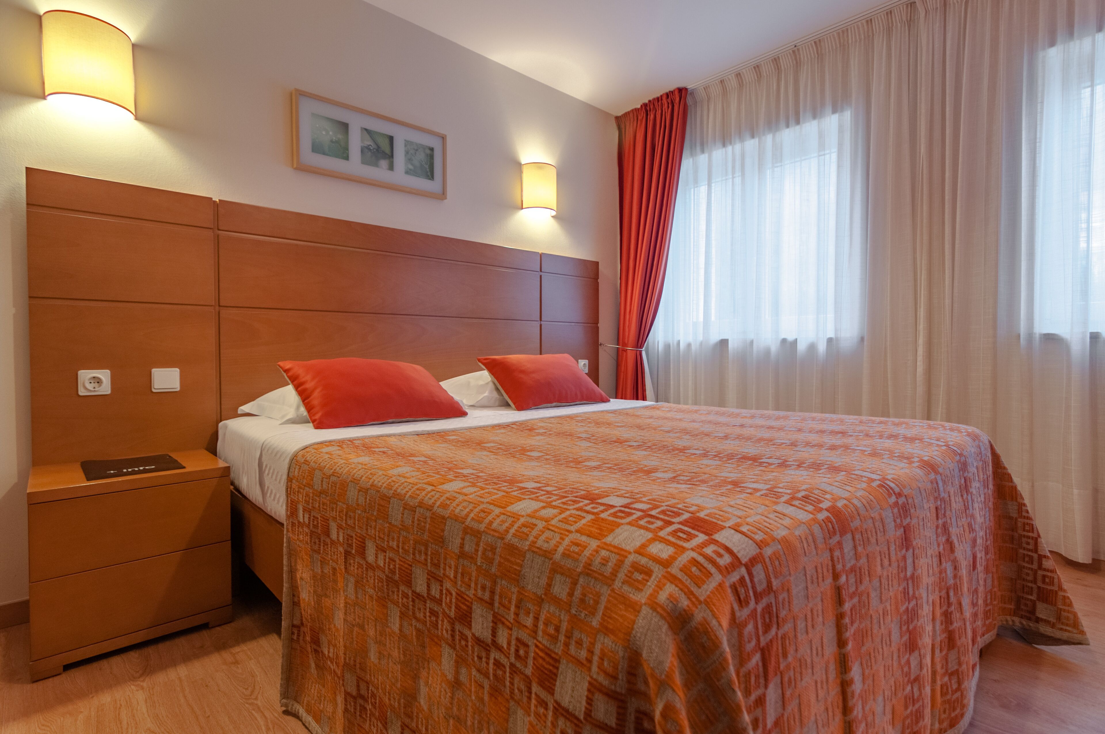 Ein Hotelzimmer mit einem großen Bett, zwei Nachttischlampen, einem Nachttisch und einem fenster mit Vorhängen.
