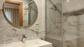 A bathroom with a marble wall, a round mirror, a sink, and a glass shower enclosure.