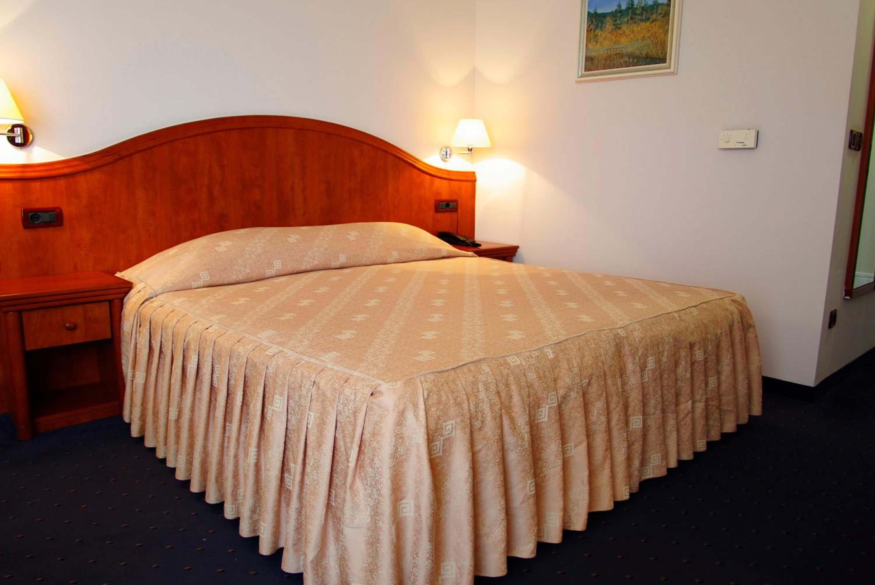 A neatly made bed with a wooden headboard, a bedside table with a lamp, and a wall-mounted light fixture.