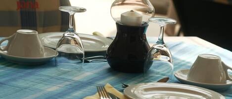 Una mesa dispuesta con platos, vasos, una vela y una botella, con mantel a cuadros.