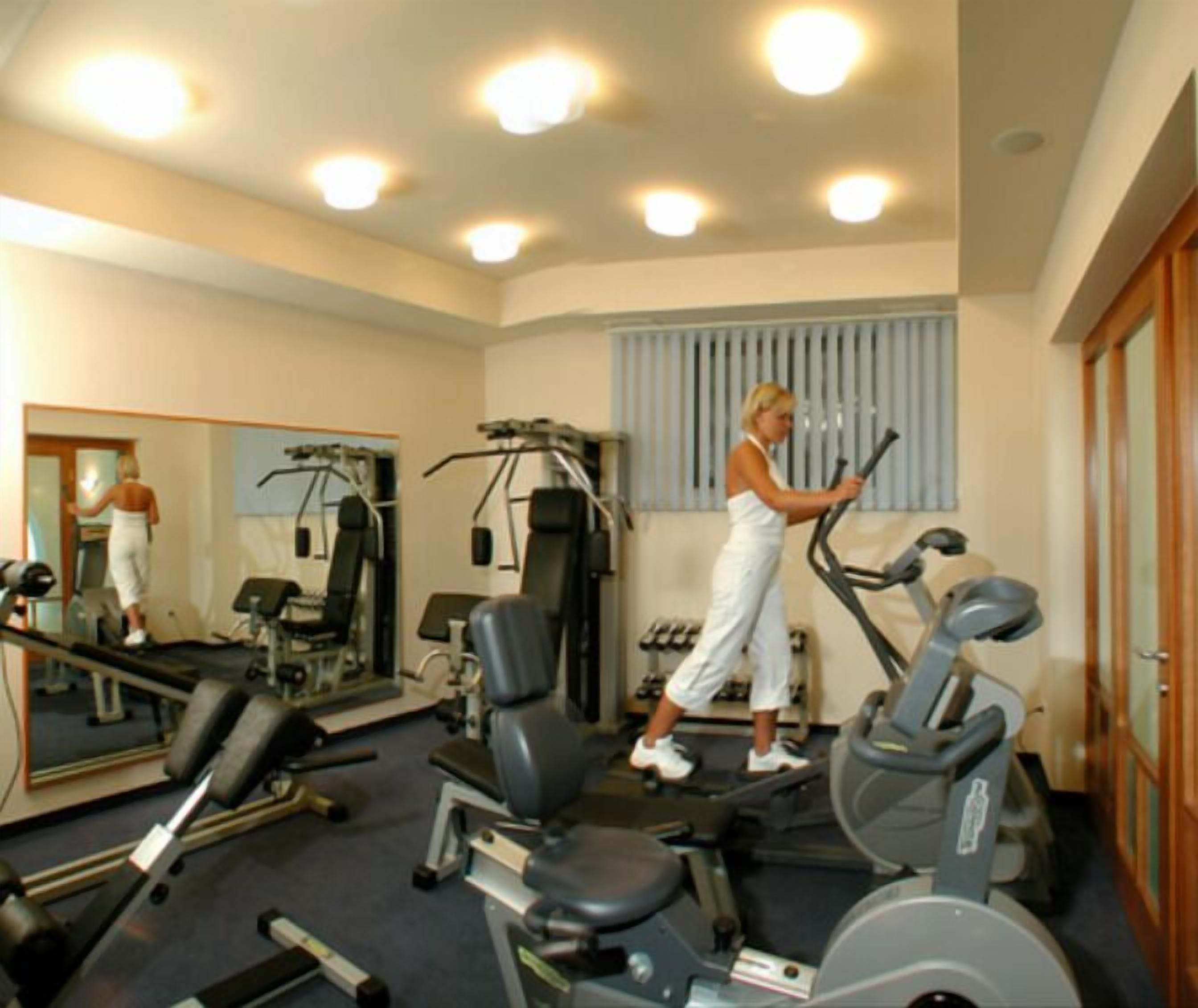 A gym with exercise equipment, a mirror, and a window with blinds.