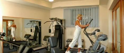 A gym with exercise equipment, a mirror, and a window with blinds.