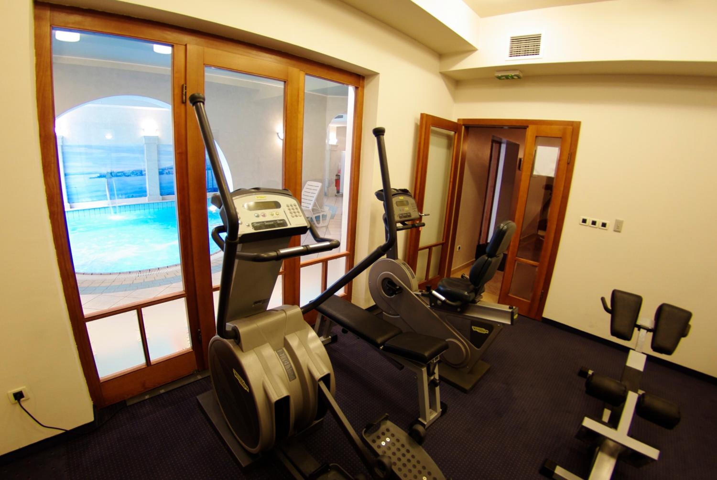 A gym with cardio machines, weight benches, and a view of a pool through glass doors.