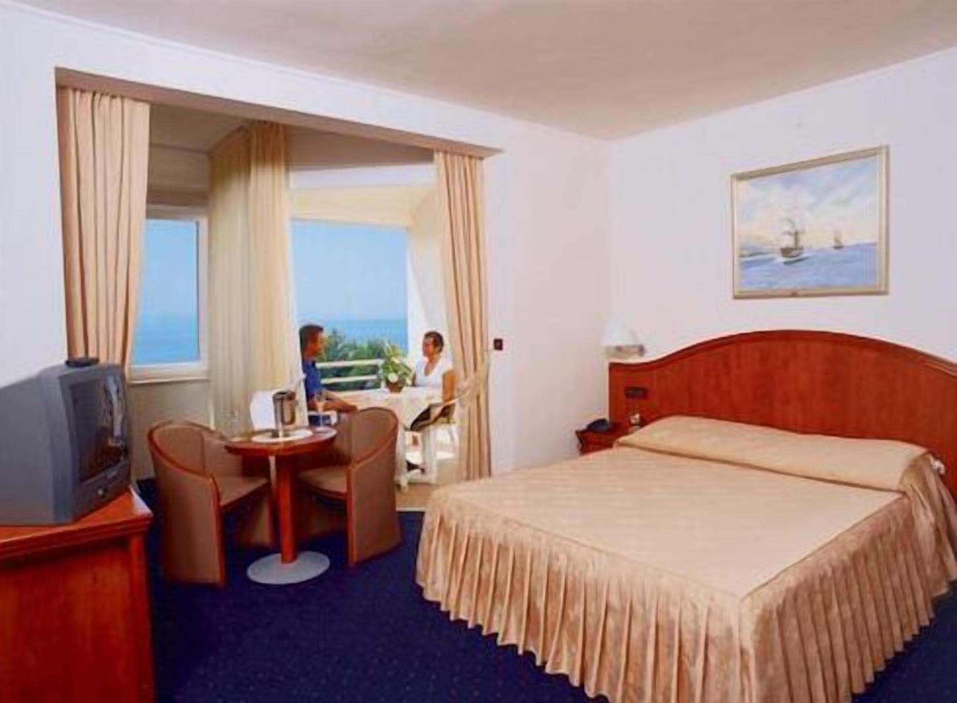 A hotel room with a bed, a desk with a chair, a television, and a window with curtains.