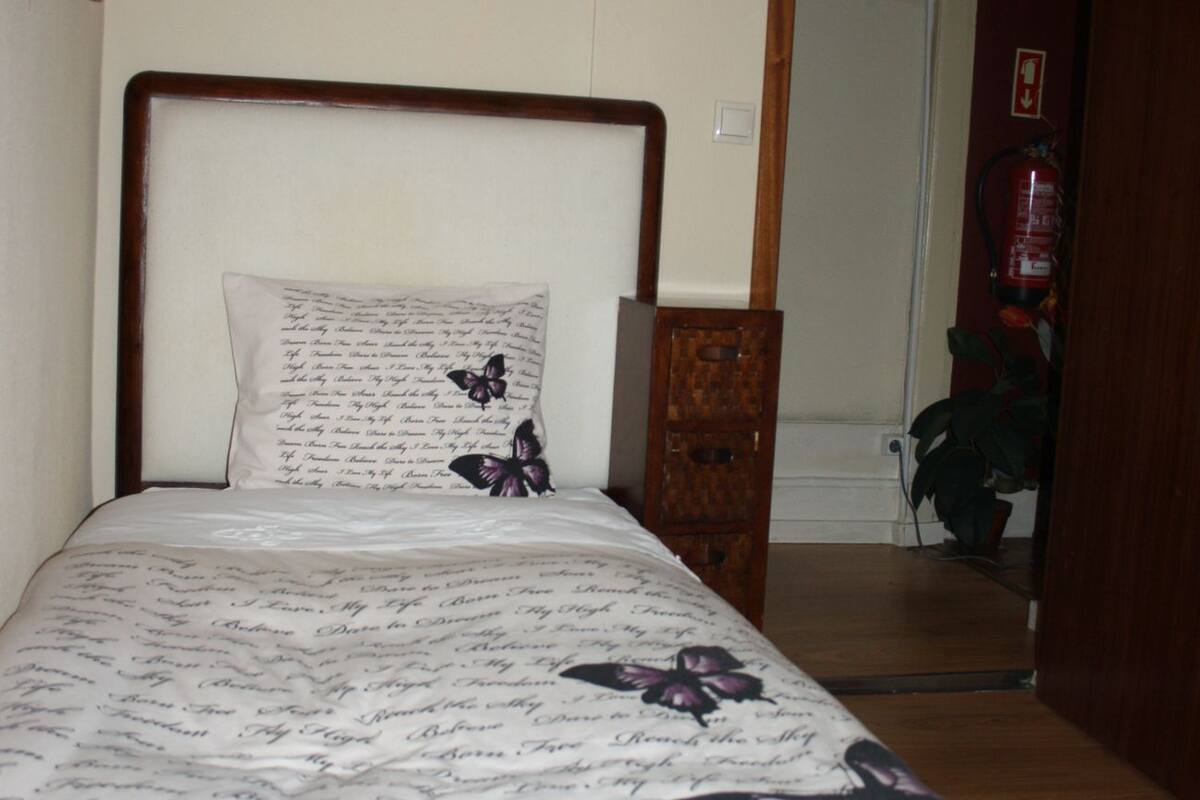 A bedroom with a wooden bed frame, a white pillow with floral patterns, and a bedside table.