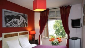 A hotel room with a bed, a painting, a window with curtains, a TV, and a vase with flowers. - Residencia Pedra Antiga (Porto)