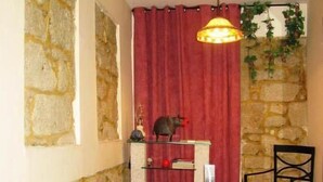 A room with a stone wall, a red curtain, a hanging plant, a chair, and a small table with a statue. - Residencia Pedra Antiga (Porto)