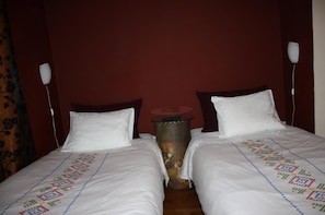 A hotel room with two single beds, each with a white pillow and a decorative bedspread. There is a small round table between the beds with a lamp on it. - Residencia Pedra Antiga (Porto)