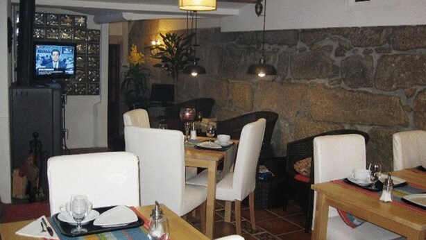 A dining area with tables set for two, white chairs, and a television mounted on the wall. - Residencia Pedra Antiga (Porto)