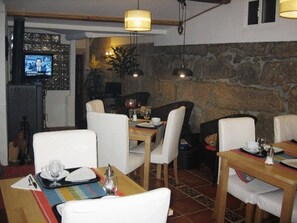 Un comedor con mesas dispuestas para dos personas, sillas blancas y un televisor montado en la pared.
