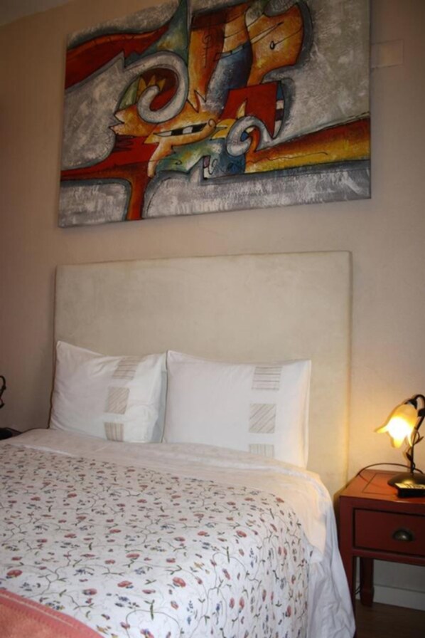 A bedroom with a bed, pillows, a nightstand with a lamp, and a colorful abstract painting on the wall. - Residencia Pedra Antiga (Porto)