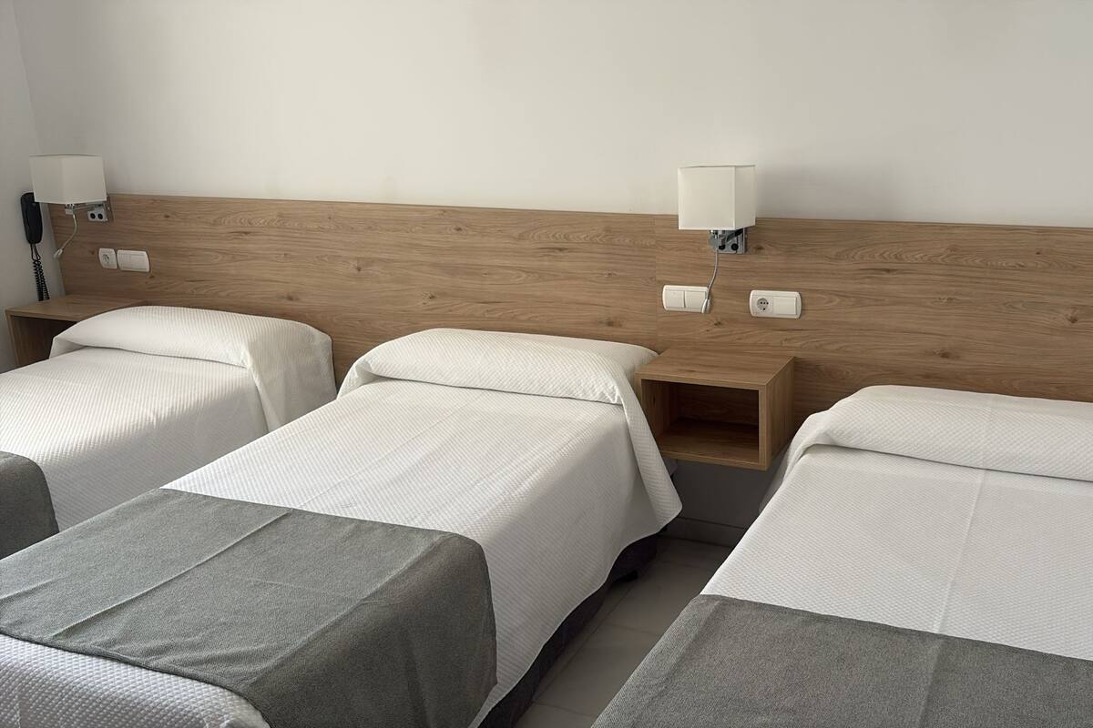 Habitación de hotel con dos camas individuales, cabecero de madera, lámparas de noche y una mesita de noche de madera.