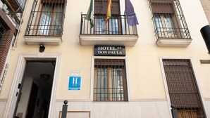 Een hotelgevel met balkons, een bord waarop 'HOTEL DON PAULA' staat en een blauw gehandicapten toegangsteken.