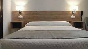 Een keurig opgemaakt bed met een houten hoofdeinde, twee nachtkastjes met lampen en een telefoon aan de rechterkant.