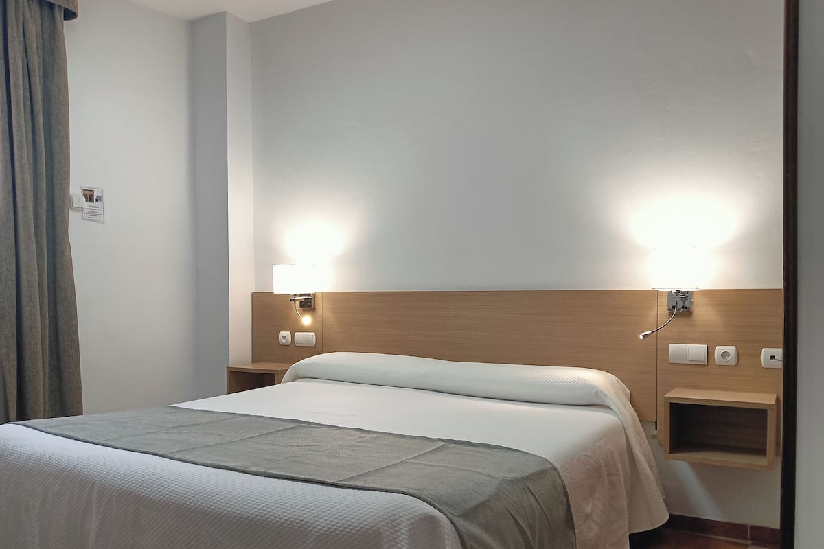 Habitación de hotel con cama, mesitas de noche e iluminación empotrada en la pared.