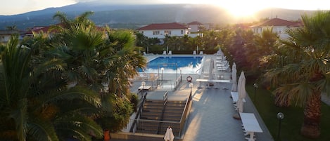A pool area with steps leading to the water, surrounded by palm trees and lounge chairs.