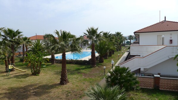 A residential area with a swimming pool, palm trees, and a white building with a red-tiled roof. - King's House Hotel Resort (Mascali)