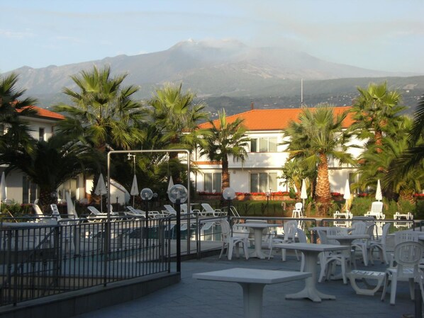 Un resort con terraza al aire libre, palmeras y vista a la montaña.
