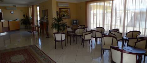 A hotel lobby with a reception desk, seating area, and a large window with curtains.