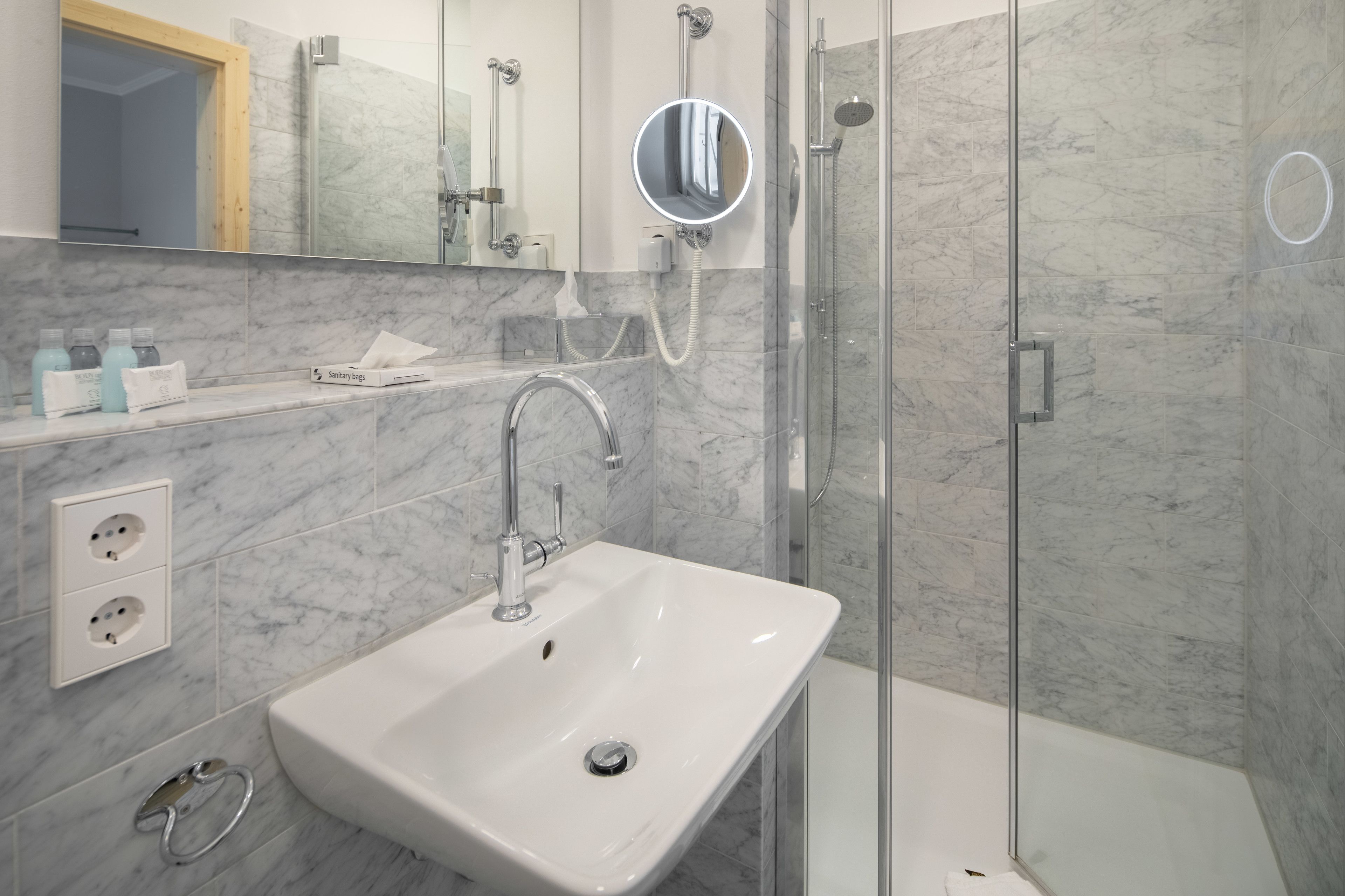 Une salle de bain moderne avec un lavabo blanc, une cabine de douche en verre et des murs en marbre.