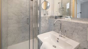 Un baño moderno con ducha envuelta en vidrio, un lavabo blanco y un espejo grande.