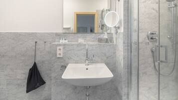 Un bany amb un lavabo blanc, un mirall, una dutxa i un escurapulides.