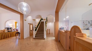 Un hall de hotel con un mostrador de recepción de madera, una escalera adornada con decoraciones festivas y una cocina al fondo.