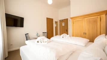 Habitación de hotel con una cama grande, un televisor de pantalla plana en la pared, armarios de madera y una mesita con una botella y una taza.