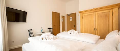A hotel room with a large bed, a flat-screen TV mounted on the wall, wooden wardrobes, and a small table with a bottle and a cup.