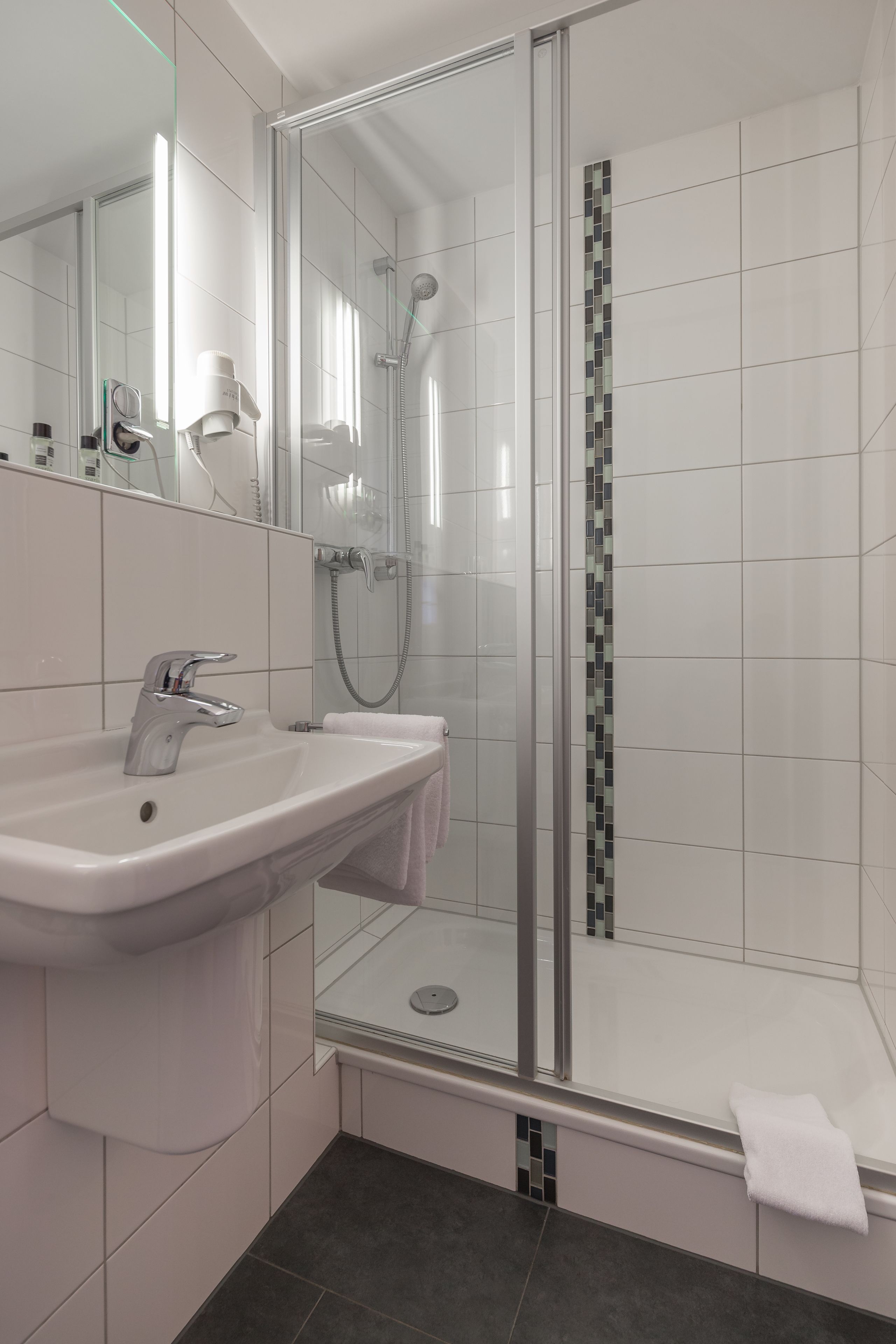 Une salle de bain moderne avec une douche à parois de verre, un lavabo blanc et un miroir.