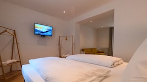 Habitación de hotel con cama, televisor montado en la pared, escalera de madera y una silla amarilla.