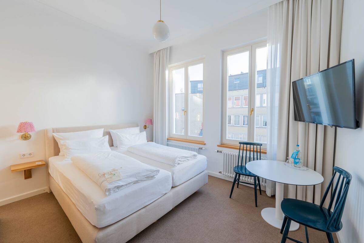 A hotel room with two beds, a TV, a small table, and a chair.