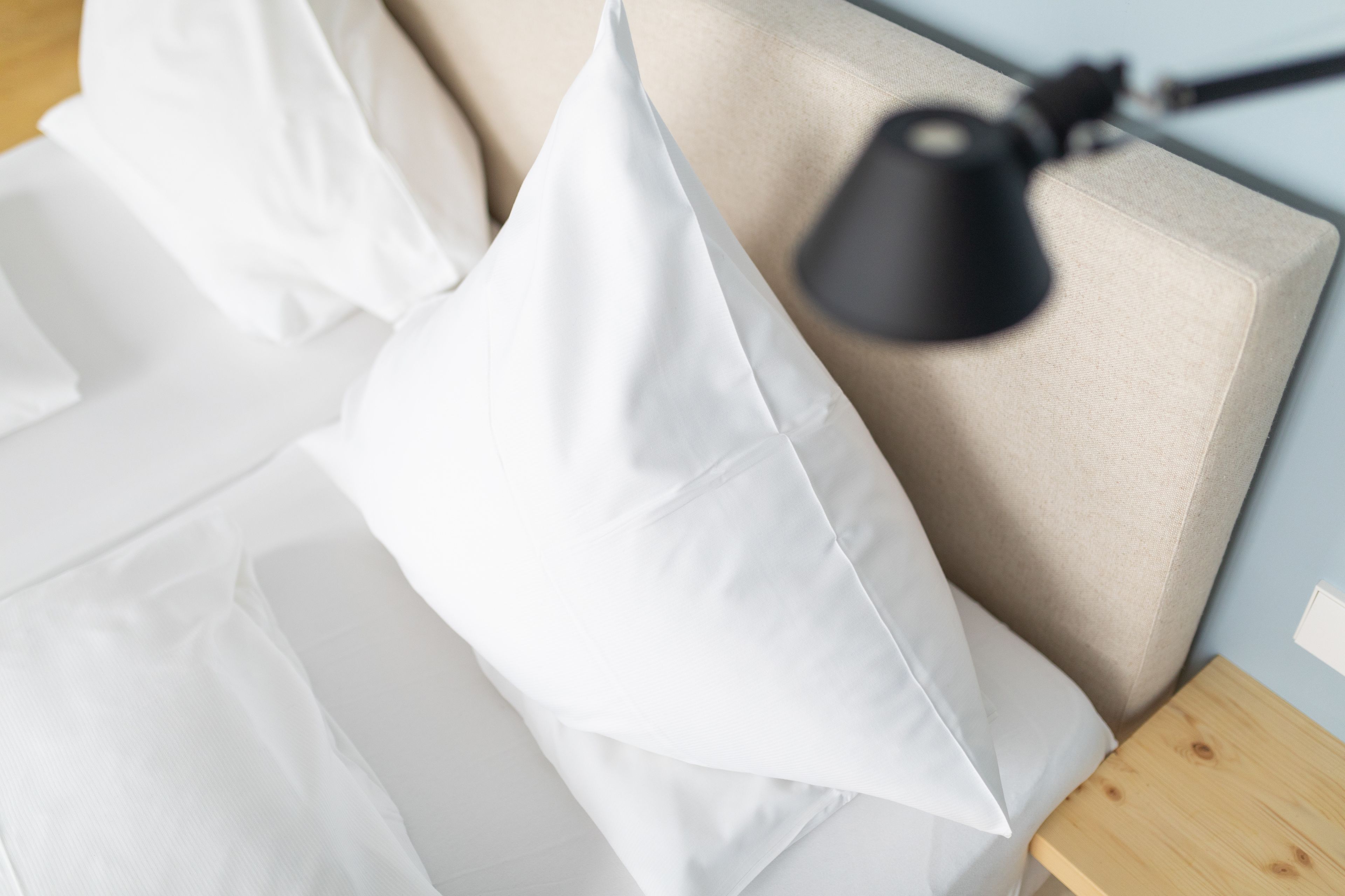 A bed with white bedding, a beige headboard, and a black lamp on a wooden nightstand.