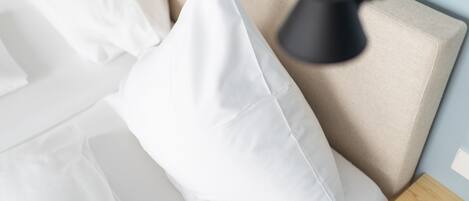 A bed with white bedding, a beige headboard, and a black lamp on a wooden nightstand.