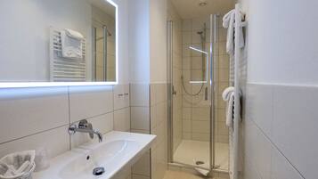 Une salle de bain moderne avec un lavabo blanc, une cabine de douche en verre et un porte-serviettes.