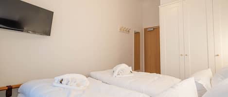 Habitació d'hotel amb dos llits, un televisor de pantalla plana penjat a la paret i un armari de fusta.