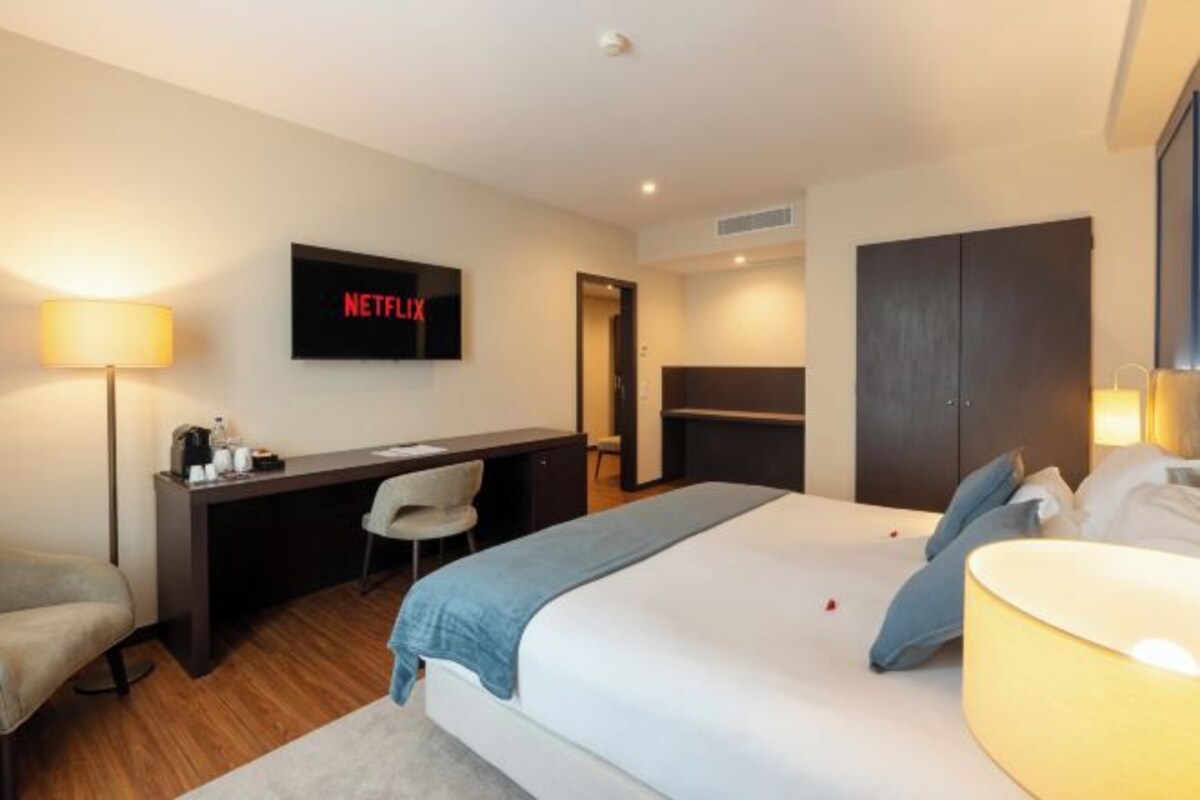 A hotel room with a bed, a desk, a chair, a TV displaying 'NETFLIX', and a wardrobe.