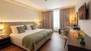 A hotel room with a bed, bedside lamps, a desk with a chair, a television, and a vase with flowers. - Premium Porto Maia (Maia)