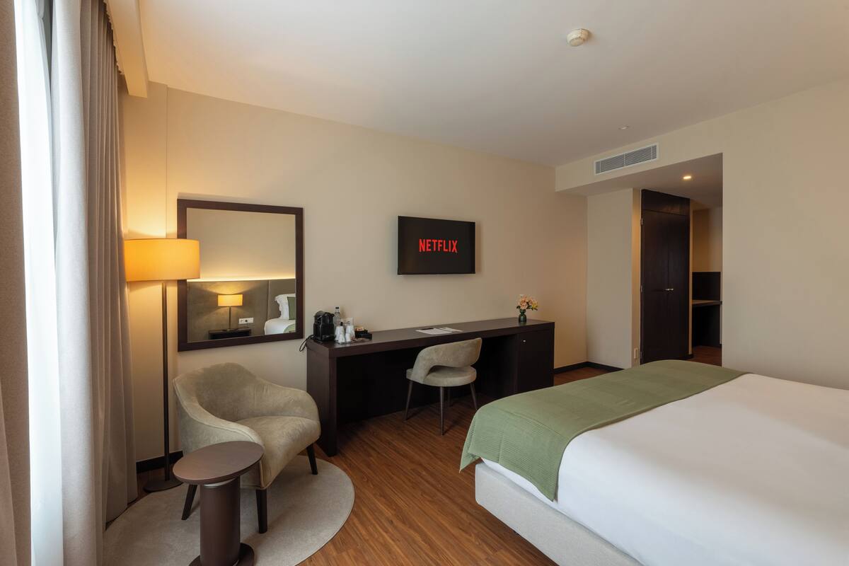 A hotel room with a bed, desk, chair, lamp, and a sign indicating a Netflix service.
