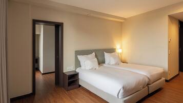 A hotel room with two beds, a nightstand, and a door leading to another room.