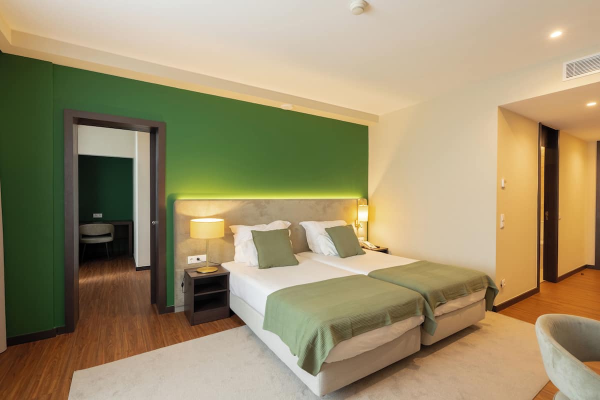 A hotel room with two beds, a desk, a chair, and a green wall.