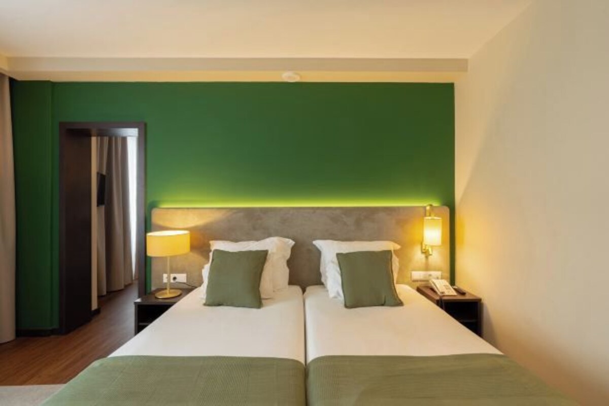A hotel room with two beds, green walls, a wooden floor, and bedside lamps.