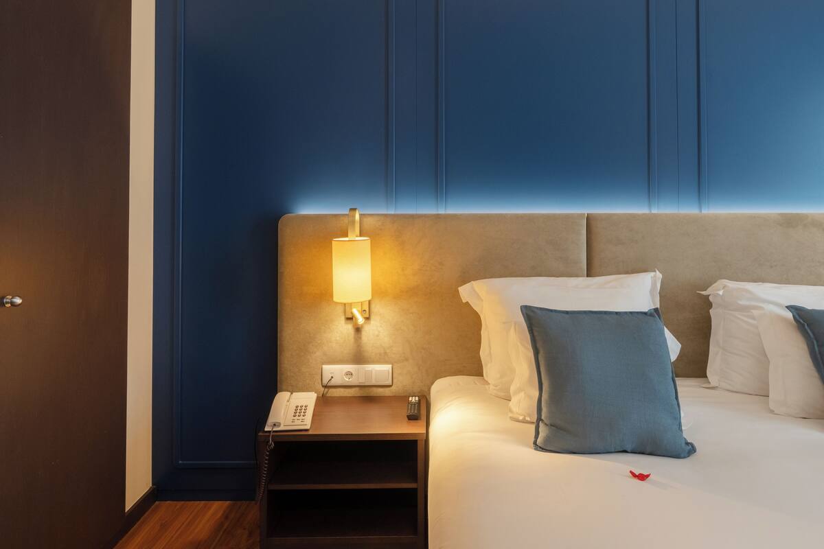 A hotel room with a bed, bedside table, lamp, and a phone.